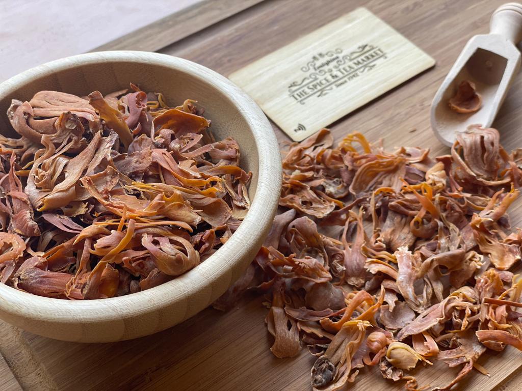 Mace blades in a wooden bowl on a wooden surface with a scoop and business card.