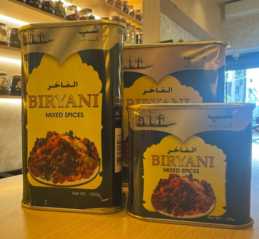 Three tins of Biryani mixed spices on a wooden surface with a blurred background.