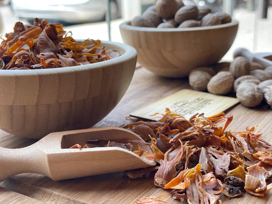 Wooden bowl with mace blades, wooden scoop, and nutmeg on a wooden surface