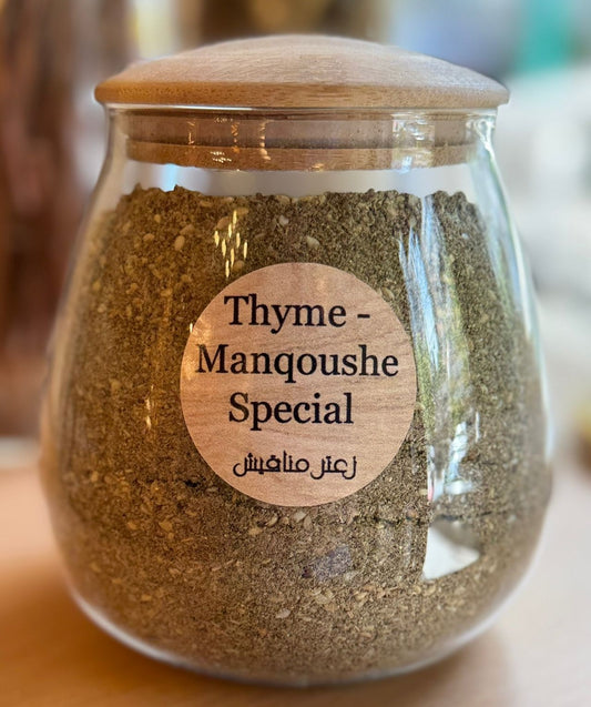 Glass jar of Thyme-Manqoushe Special spice blend with wooden lid on a blurred background