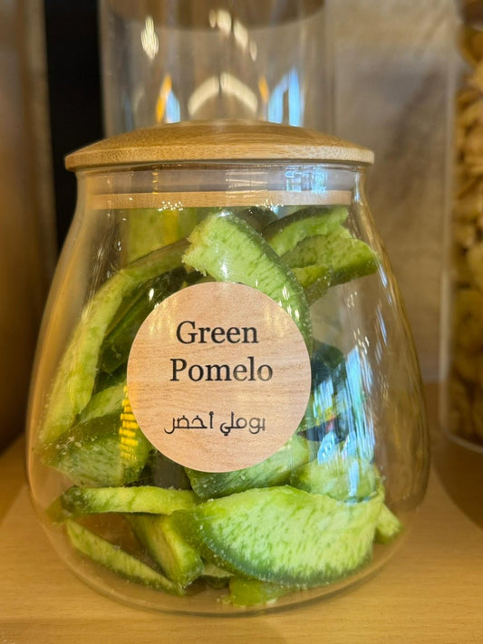 Glass jar with green pomelo slices and a wooden lid on a wooden surface.