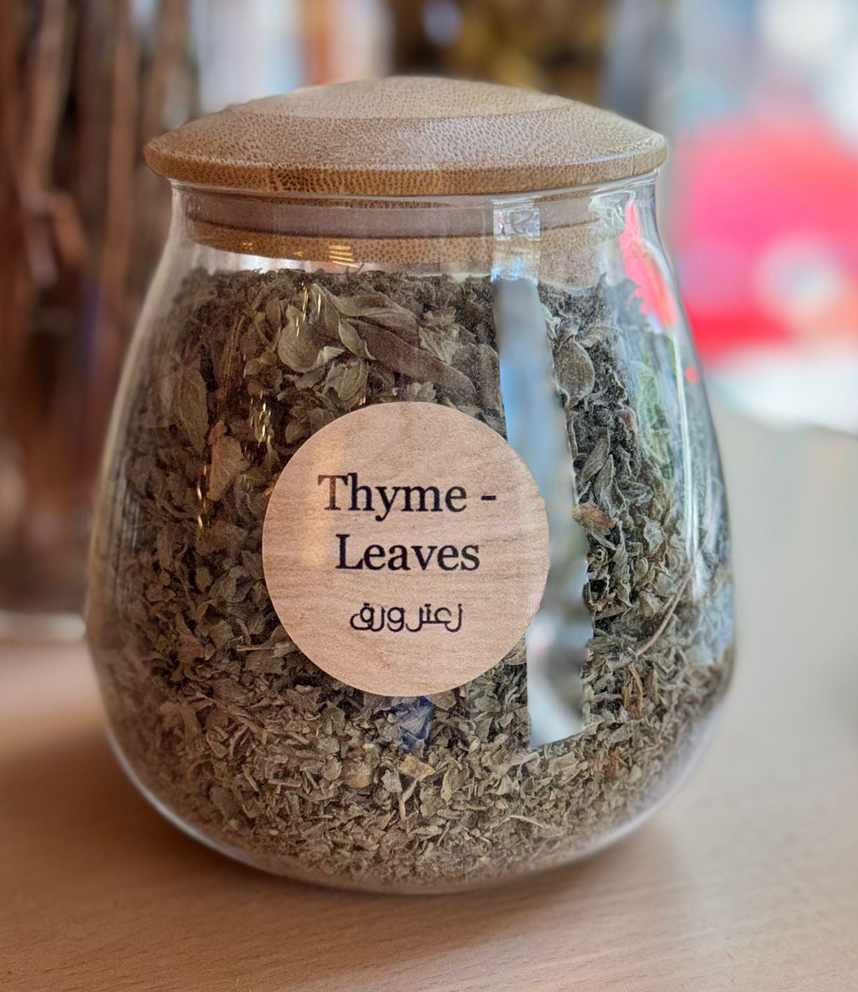Glass jar with wooden lid containing thyme leaves on a wooden surface