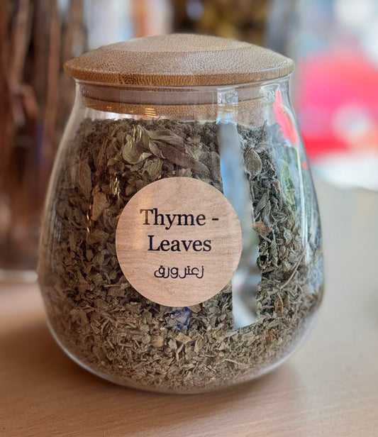 Glass jar with wooden lid containing thyme leaves on a wooden surface